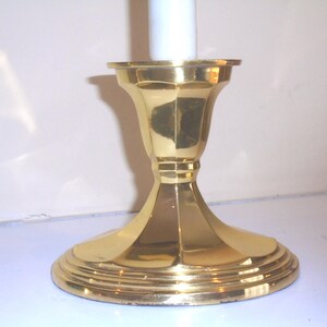 Puede incluir: Un candelero de lat&oacute;n pulido con una base ancha y escalonada y un cuerpo acanalado en forma de campana. El candelero est&aacute; dise&ntilde;ado para sostener una sola vela blanca. El dise&ntilde;o general es cl&aacute;sico y elegante.