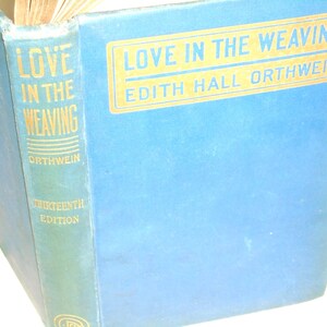 May include: A vintage book titled "Love in the Weaving" by Edith Hall Orthwein. The book has a light blue cover with gold lettering. The spine is a darker blue-green with the title and author's name.