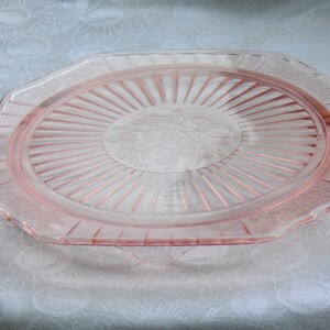 Puede incluir: Una bandeja de servir de cristal rosa con un dise&ntilde;o floral en el centro. La bandeja tiene forma rectangular con bordes festoneados y asas a cada lado. La bandeja es de cristal transparente y tiene un aspecto delicado y vintage.