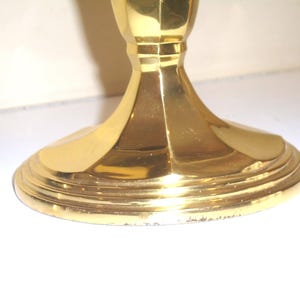 Puede incluir: Un candelero dorado con una base ancha y escalonada y un tallo acanalado. La base tiene una serie de anillos conc&eacute;ntricos y el tallo tiene un dise&ntilde;o facetado. El candelero est&aacute; hecho de un material brillante y reflectante.