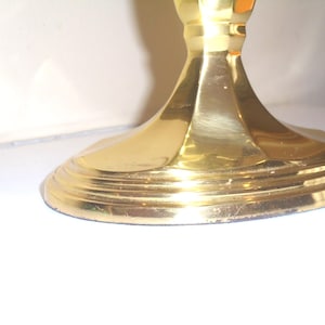 Puede incluir: Primer plano de una base de candelabro dorada. La base tiene un dise&ntilde;o redondo y escalonado con un tallo acanalado. El metal tiene un acabado pulido, que refleja la luz. El candelabro es probablemente para uso decorativo.