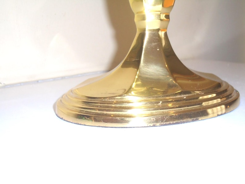 Puede incluir: Primer plano de una base de candelabro dorada. La base tiene un dise&ntilde;o redondo y escalonado con un tallo acanalado. El metal tiene un acabado pulido, que refleja la luz. El candelabro es probablemente para uso decorativo.