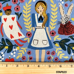 May include: Blue fabric with a whimsical Alice in Wonderland print featuring Alice, the Queen of Hearts, the White Rabbit, and various floral and foliage designs.