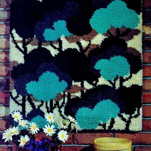 May include: A wall hanging with a tufted texture depicting a forest scene with blue, brown, and white trees. The hanging is made of yarn and is mounted on a brick wall.
