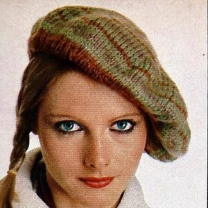 Peut inclure: Une femme aux longs cheveux blonds porte un pull blanc &agrave; col et &agrave; bouton. Elle porte &eacute;galement un b&eacute;ret en tricot vert et marron.