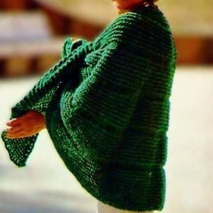 May include: A woman wearing a green knitted sweater with a loose fit. The sweater has a textured knit pattern and is worn over a white shirt.