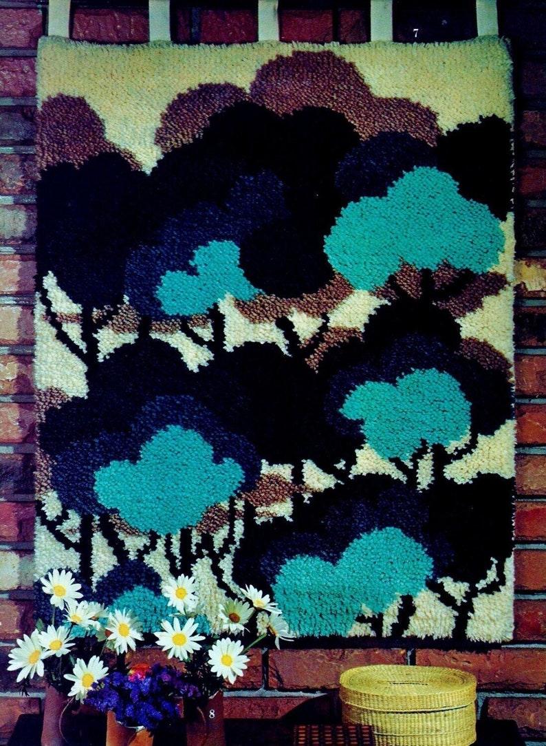 May include: A wall hanging with a tufted texture depicting a forest scene with blue, brown, and white trees. The hanging is made of yarn and is mounted on a brick wall.