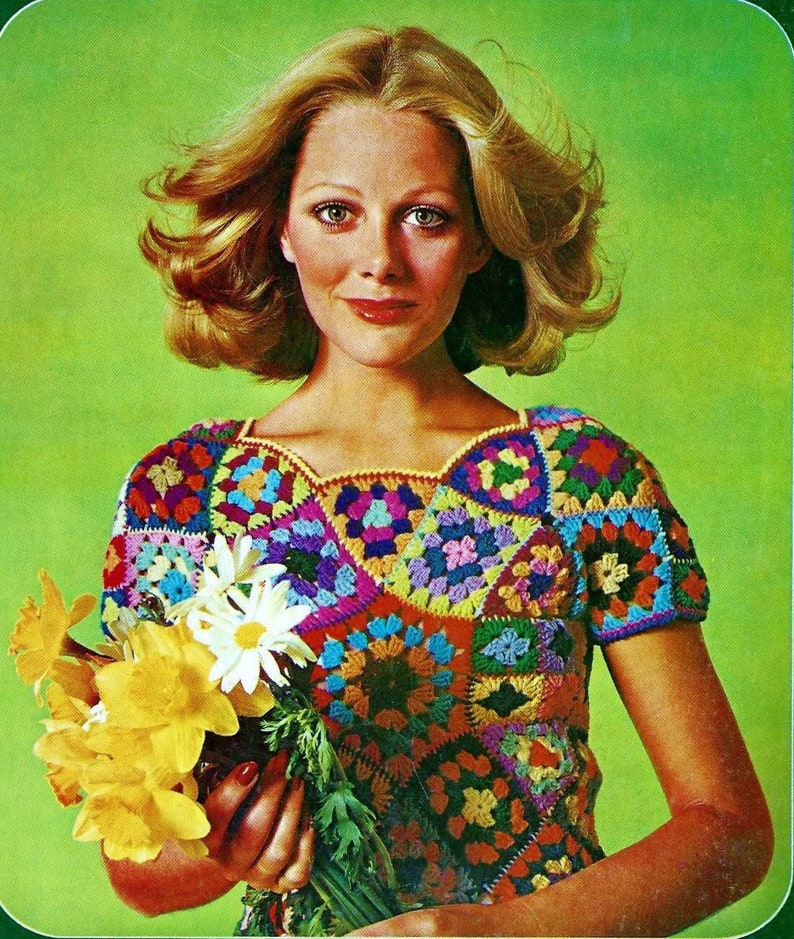 Puede incluir: Una mujer lleva una blusa de crochet de colores con un patr&oacute;n de cuadrados de la abuela. Est&aacute; sosteniendo un ramo de narcisos amarillos.