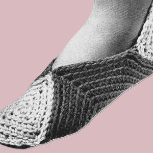 May include: A black and white crocheted slipper, with a light-colored heel and toe, and a darker, textured body. The slipper is shown on a foot, with a pink background.