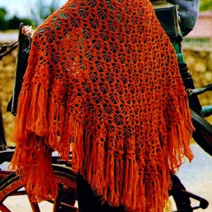 May include: A bright orange crocheted shawl with fringe. The shawl is made with a delicate open stitch pattern.