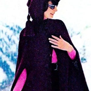 Könnte beinhalten: Ein dunkelvioletter Kapuzenmantel mit strukturierter Optik. Der Umhang wird über einem rosa Langarm-Top getragen. Die Person trägt eine Sonnenbrille. Der Hintergrund ist eine verschneite Winterszene.