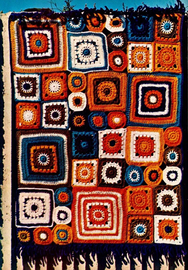 May include: A colorful crocheted blanket with a patchwork design featuring squares and circles in shades of orange, brown, blue, and white. The blanket has a fringe border.