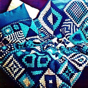 May include: A crocheted throw blanket with a geometric pattern in shades of blue, white, and black. The blanket is made with a variety of stitches and textures, creating a unique and interesting design.