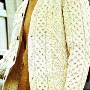 Puede incluir: Un cárdigan blanco de punto de cable con cierre de botones y un bolsillo en la parte delantera. El cárdigan está hecho de un hilo suave y texturizado.