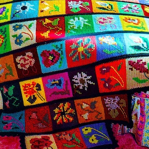 May include: A colorful crocheted blanket with a variety of floral patterns in shades of red, blue, green, yellow, and purple.