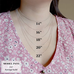 K&ouml;nnte beinhalten: Ein Model tr&auml;gt verschiedene silberne Kettenhalsb&auml;nder in unterschiedlichen L&auml;ngen von 14 bis 22 Zoll. Das Model tr&auml;gt eine rosa Bluse mit Blumenmuster und hat eine durchschnittliche Statur. Der Text "MODEL INFO" und "5'3" Average build" ist am unteren Rand des Bildes sichtbar.