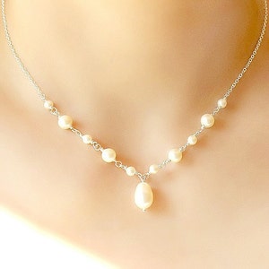 May include: A delicate silver chain necklace with a single teardrop pearl pendant and small round pearls along the chain.