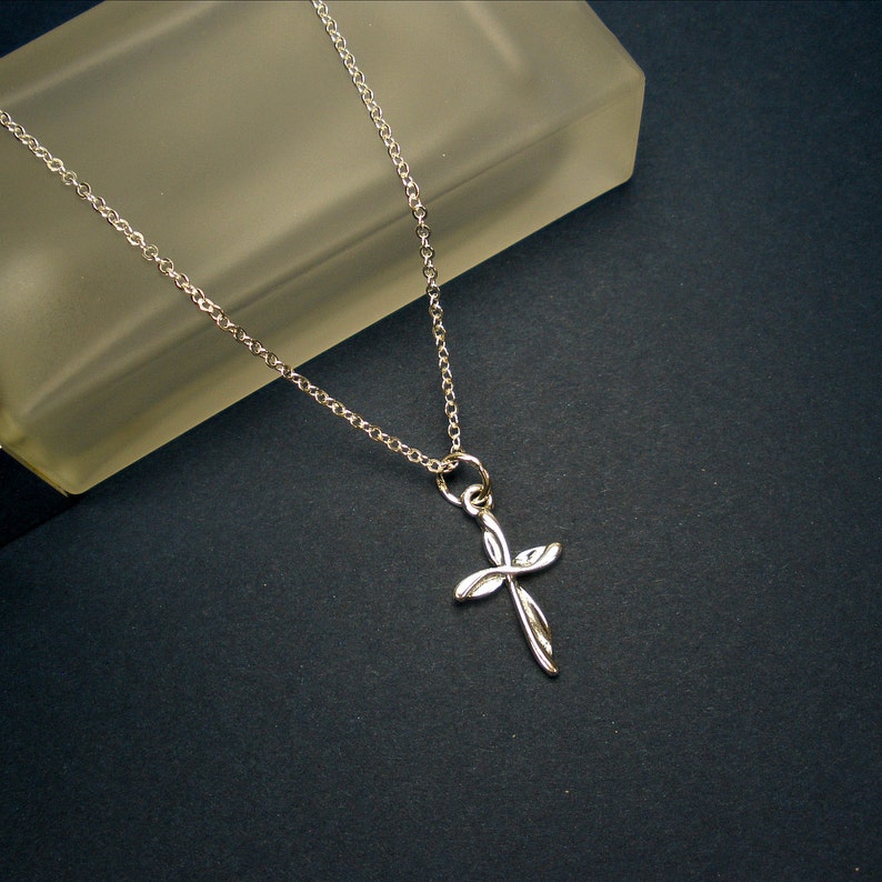 May include: A silver chain necklace with a delicate, twisted cross pendant.