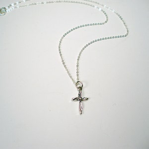 May include: A silver chain necklace with a small, twisted silver cross pendant.