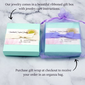 K&ouml;nnte beinhalten: Zwei hellblaue Geschenkboxen mit wei&szlig;en Deckeln und einem Blumendesign. Die Boxen haben ein wei&szlig;es Band und den Text "Handmade Custom Jewelry" und "StarringYouJewelry.com Made in USA". Die Boxen stehen auf einer wei&szlig;en Oberfl&auml;che. Die Boxen sind von einem hellvioletten Organzasack umgeben.