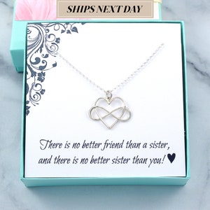 May include: A silver necklace with a heart and infinity symbol pendant, presented in a teal gift box. The card inside reads, "There is no better friend than a sister, and there is no better sister than you!" The box has a floral design.