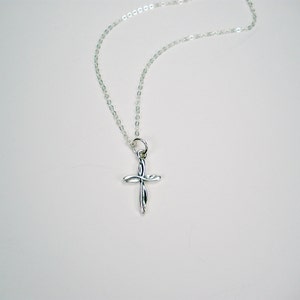 May include: A silver chain necklace with a small, silver cross pendant. The cross is a simple design with a twisted or knotted look.