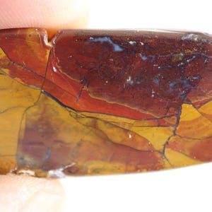 May include: A polished, rectangular-shaped piece of jasper stone featuring a complex pattern of deep maroon, ochre yellow, and dark brown colors with visible black veining and fractures running across the smooth, glossy surface of the mineral.