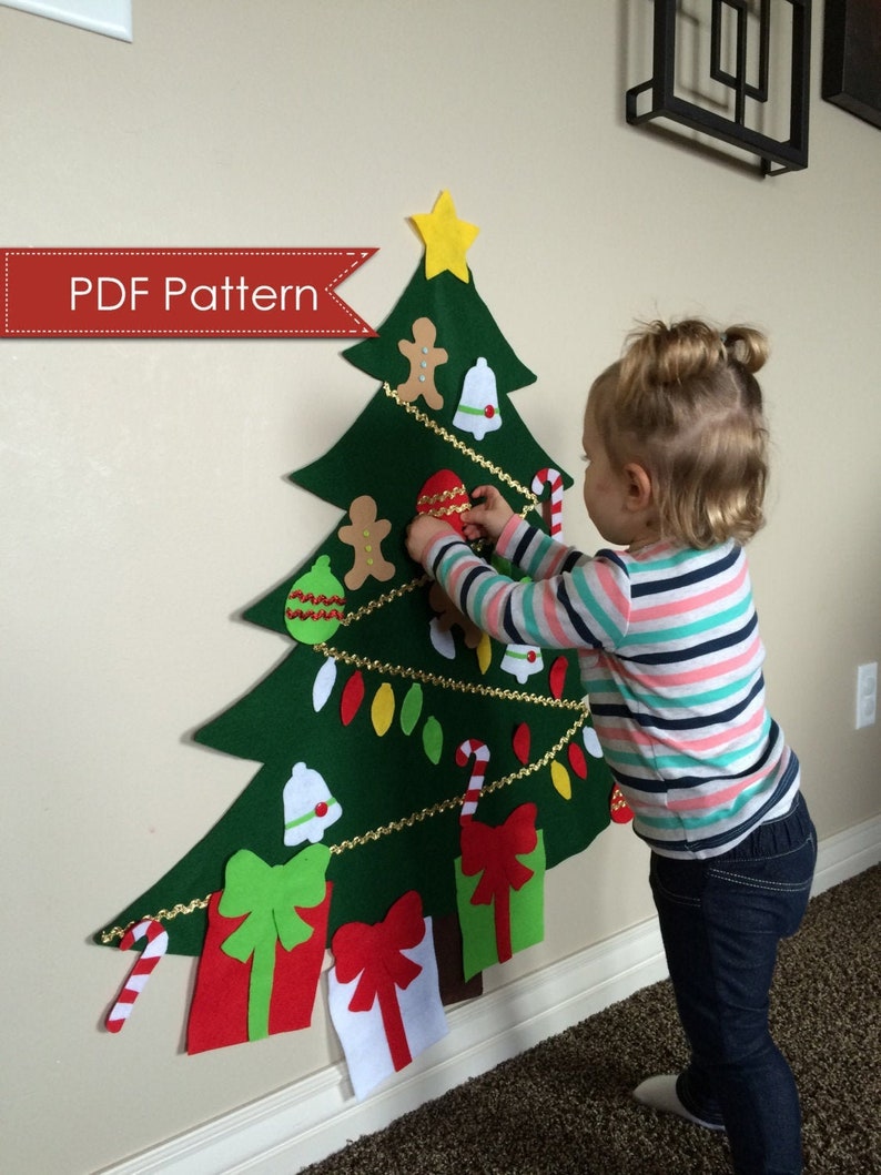 May include: A felt Christmas tree with a star on top, decorated with ornaments, gingerbread men, candy canes, and presents. A child is decorating the tree.