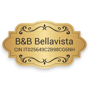 Può includere: Una targhetta dorata con la scritta "B&B Bellavista" e un codice identificativo univoco. La targhetta ha un bordo decorativo con disegni a spirale. Lo sfondo è bianco.