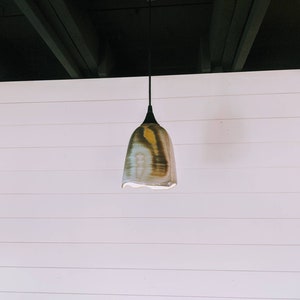 May include: A ceramic pendant light fixture with a brown, white, and yellow glaze. The light fixture is hanging from a black cord against a white wall.