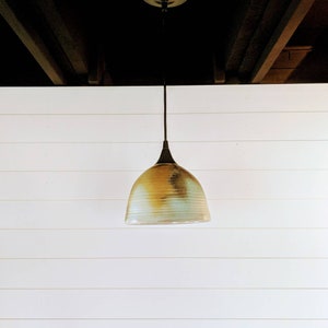 May include: A hanging light fixture with a brown and white ceramic shade. The shade has a mottled, textured finish.