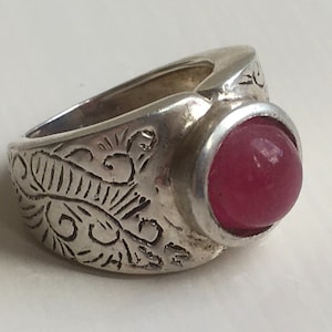 May include: A silver ring with an ornate design and a large, round, pink gemstone.