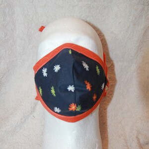 May include: A black face mask with a white and orange floral pattern. The mask has an orange border and ties.