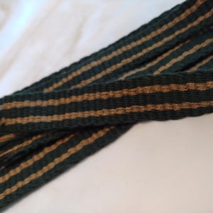 Puede incluir: Una tela tejida a rayas verdes y marrones con un borde con flecos.
