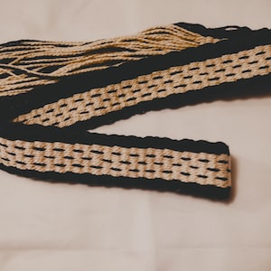 Puede incluir: Un cinturón tejido negro y crema con flecos en un extremo.