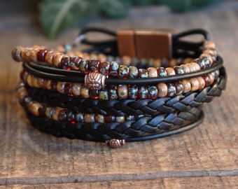 May include: A multi-layered bracelet with black leather and brown, red, and white beads. The bracelet has a braided leather strap and a copper clasp.