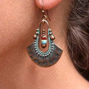 May include: A copper-coloured earring with a fan-shaped design and turquoise accents. The earring features a textured surface and a dangling section with colourful beads. The earring is a unique piece of jewellery.