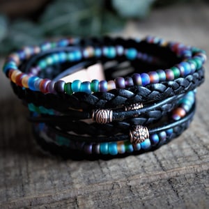 May include: A multi-strand bracelet with black leather cord and iridescent glass beads. The bracelet has two copper accents with a decorative design.