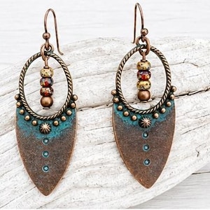 May include: A pair of dangle earrings featuring a copper-toned teardrop-shaped pendant with a teal patina finish, accented by small metal studs and three vertical dots. A twisted metal hoop hangs above, holding three small multicolored beads.