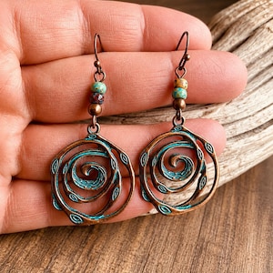 May include: Copper-toned spiral earrings with turquoise detailing. Each earring showcases a spiral design with a turquoise outline and small turquoise and brown beads. The earrings have a hook fastening.
