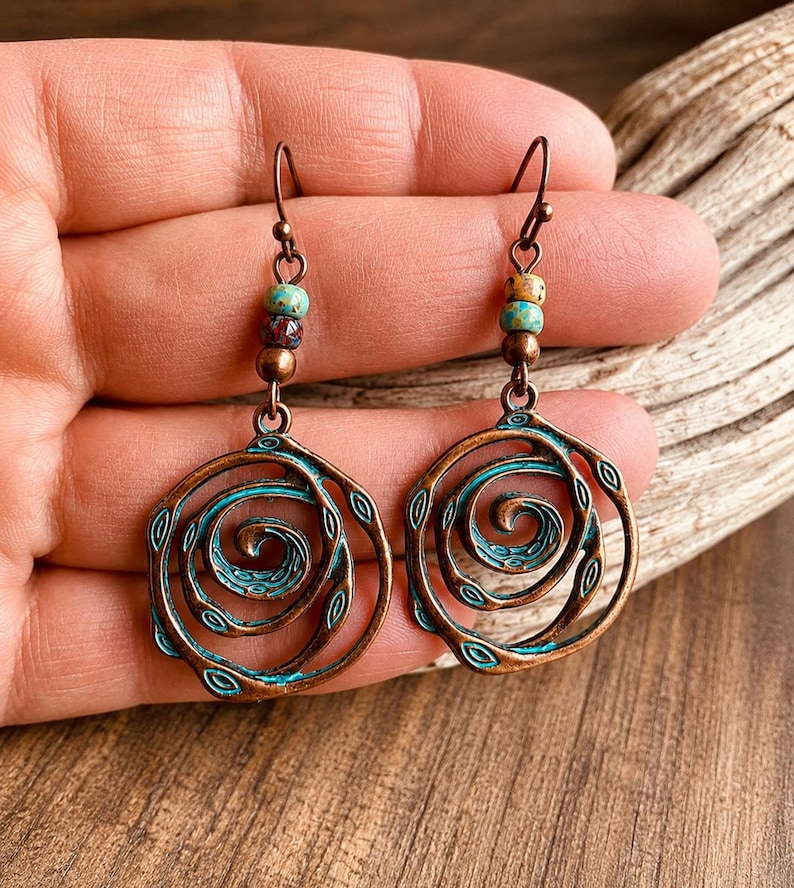 May include: Copper-toned spiral earrings with turquoise detailing. Each earring showcases a spiral design with a turquoise outline and small turquoise and brown beads. The earrings have a hook fastening.