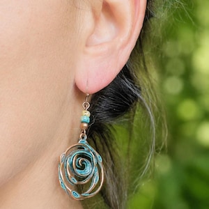 May include: Copper-coloured spiral earrings with turquoise accents. The earrings have a floral design and are suspended from a small hook. The earrings are a unique piece of jewellery.