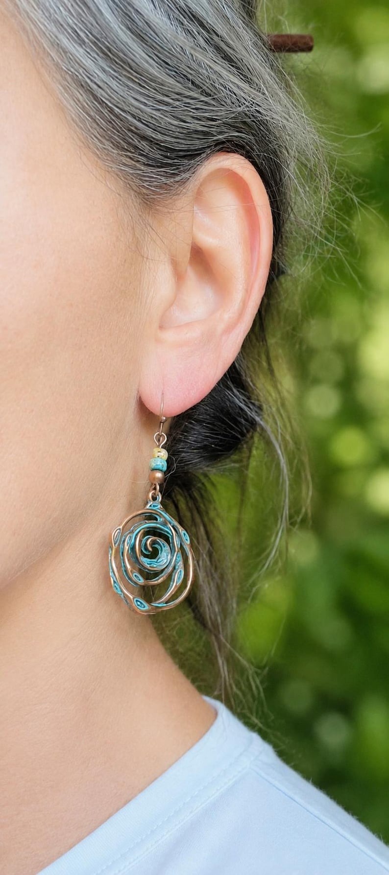 May include: Copper-coloured spiral earrings with turquoise accents. The earrings have a floral design and are suspended from a small hook. The earrings are a unique piece of jewellery.