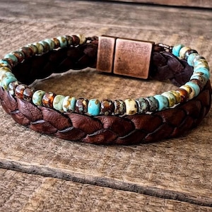 Braided brown leather bracelet with turquoise and brown beaded accents. The bracelet features a copper-colored magnetic clasp. A stylish accessory for everyday wear.
