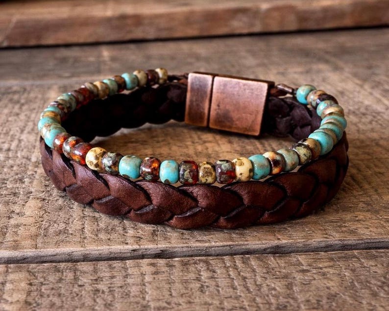 Braided brown leather bracelet with a turquoise and brown beaded accent. The bracelet features a copper-colored magnetic clasp. The design is rustic and casual, suitable for everyday wear.