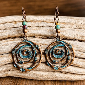 May include: A pair of copper-coloured earrings with a spiral design. The earrings have a turquoise and bronze finish, with colourful beads at the top. The earrings are displayed on a wooden surface.