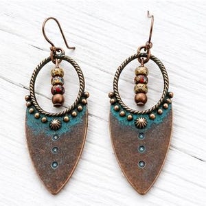 May include: A pair of dangle earrings featuring a copper-toned teardrop-shaped pendant with a teal patina finish, accented by a row of small metal studs and three circular indentations. A twisted metal hoop holds three multi-colored beads.