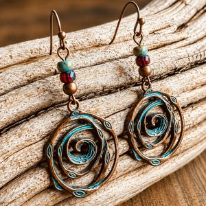 May include: Copper-coloured earrings with a spiral design. The earrings have a turquoise and red beaded accent above the spiral. The spiral design is outlined in turquoise and has small oval cutouts. The earrings hang from a copper-coloured hook.