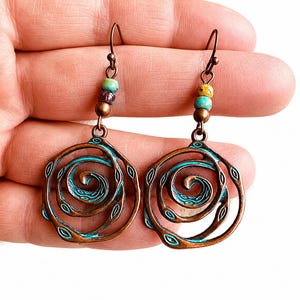 May include: A pair of copper-coloured spiral earrings with turquoise accents. Each earring features a spiral design with small, colourful beads at the top. The earrings are designed with a hook closure.