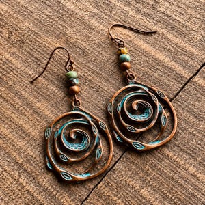 May include: Copper-coloured spiral earrings with turquoise accents and small beads. The earrings have a unique, artistic design with a rustic, bohemian aesthetic. The spiral design is accented with small leaf shapes.